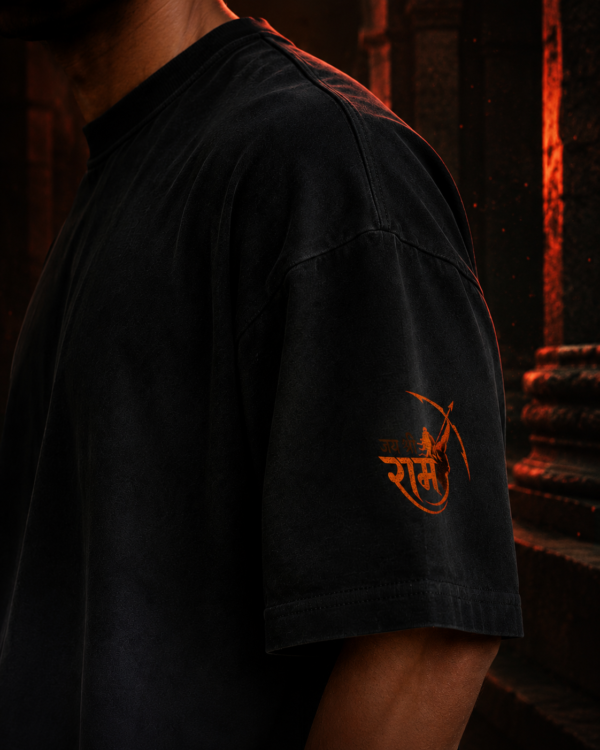 Close up of the right sleeve on the black ombré t-shirt displaying the orange Lord Rama bow graphic and Jai Shri Ram text.